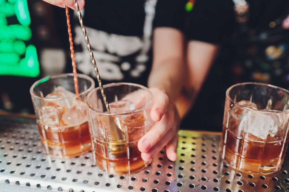 manos de barman preparando combinado en vaso de whisky con hielo