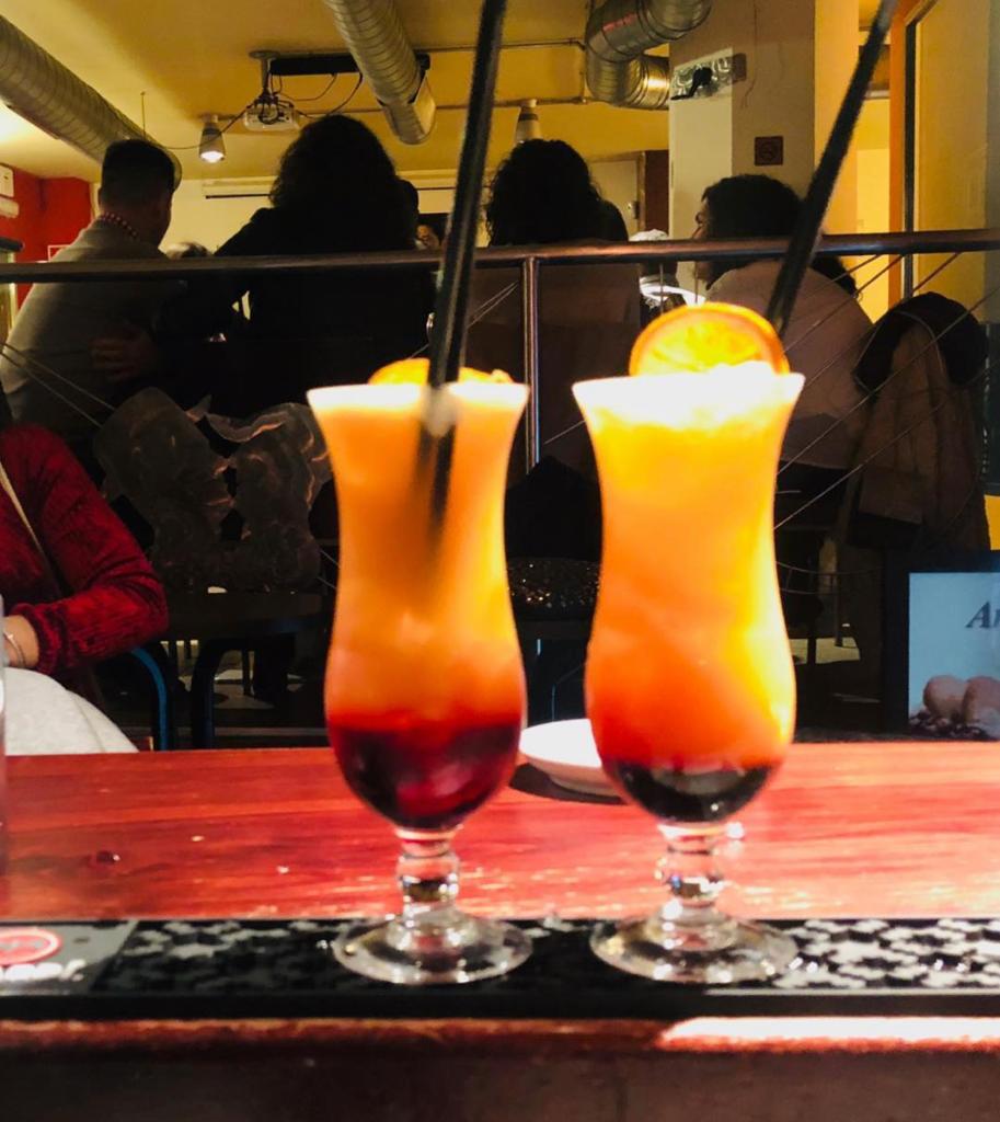 CAFÉ BAR D´BENIS dos cocteles sobre barra con siluetas de gente sentada de fondo